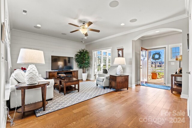 living room featuring ceiling fan, wood walls, crown molding, and light hardwood / wood-style flooring