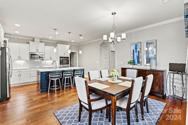 dining room with light hardwood / wood-style floors, ornamental molding, sink, and a chandelier