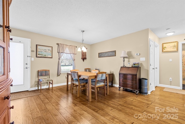 dining area with light hardwood / wood-style floors, a textured ceiling, and a notable chandelier