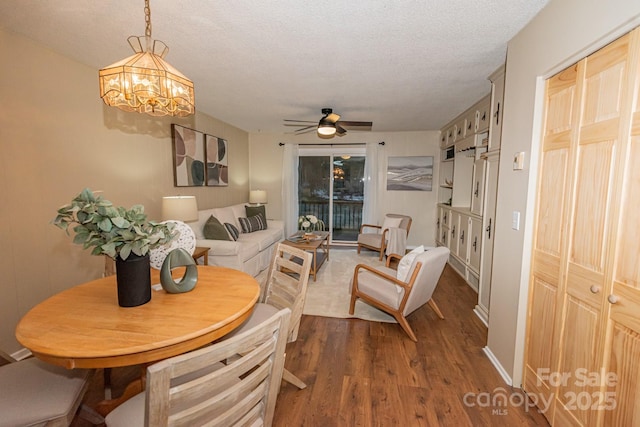 dining space with a textured ceiling, ceiling fan with notable chandelier, and dark hardwood / wood-style floors