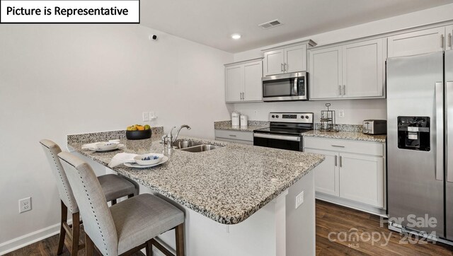 kitchen featuring a kitchen breakfast bar, sink, dark hardwood / wood-style floors, appliances with stainless steel finishes, and light stone counters