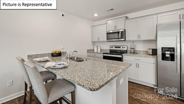 kitchen with light stone countertops, stainless steel appliances, dark wood-type flooring, sink, and a breakfast bar area