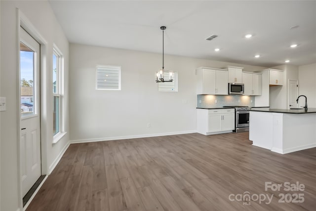 kitchen featuring stainless steel appliances, hanging light fixtures, hardwood / wood-style floors, white cabinets, and decorative backsplash