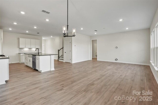 kitchen with a center island with sink, light hardwood / wood-style flooring, pendant lighting, white cabinets, and tasteful backsplash