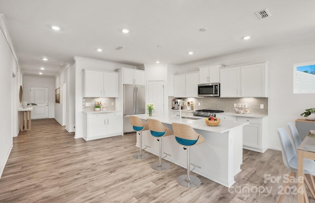 kitchen featuring appliances with stainless steel finishes, light wood-type flooring, sink, white cabinetry, and an island with sink