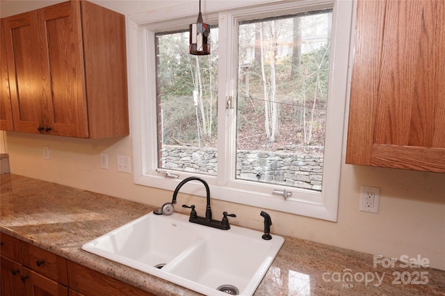 kitchen featuring a sink, light countertops, brown cabinetry, and hanging light fixtures