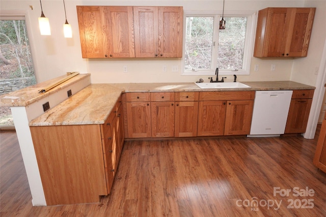 kitchen featuring dishwasher, a sink, a peninsula, wood finished floors, and pendant lighting