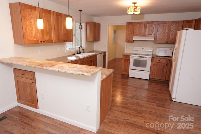 kitchen featuring white appliances, a peninsula, under cabinet range hood, dark wood finished floors, and a sink
