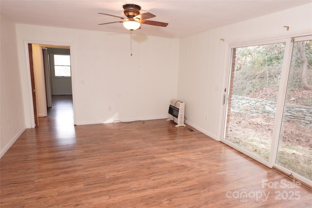 spare room with light wood-style flooring, baseboards, a ceiling fan, and heating unit