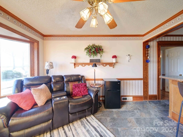 living room with ceiling fan, ornamental molding, and a textured ceiling