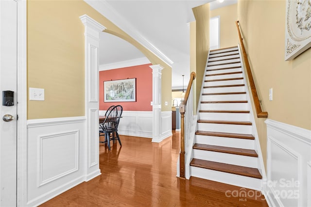 stairs with hardwood / wood-style floors, decorative columns, and crown molding