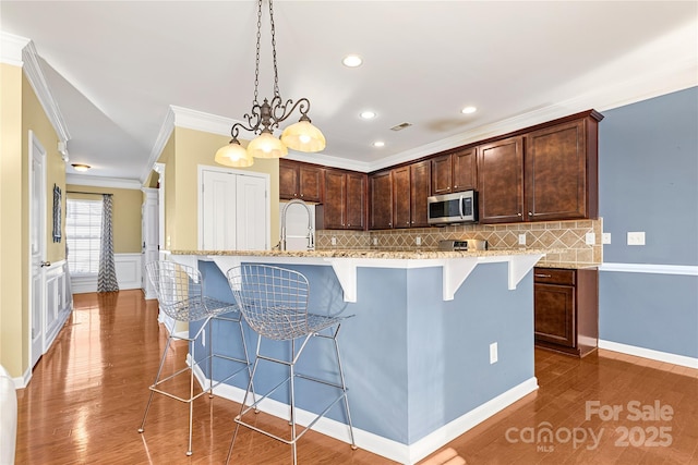 kitchen with decorative backsplash, a kitchen breakfast bar, crown molding, decorative light fixtures, and an island with sink