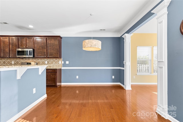 kitchen with dark brown cabinetry, tasteful backsplash, a kitchen breakfast bar, crown molding, and pendant lighting