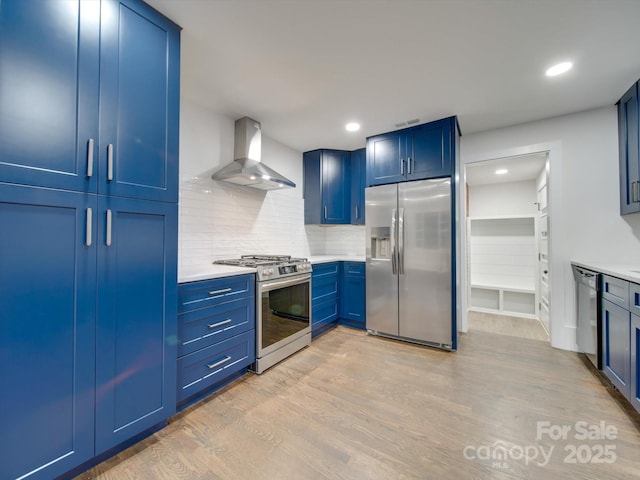 kitchen with light hardwood / wood-style floors, wall chimney range hood, stainless steel appliances, and blue cabinets