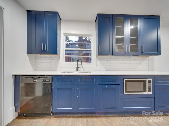 kitchen with appliances with stainless steel finishes, tasteful backsplash, blue cabinets, sink, and light hardwood / wood-style floors