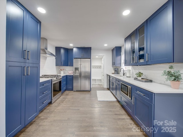 kitchen featuring light hardwood / wood-style flooring, stainless steel appliances, wall chimney exhaust hood, and blue cabinets