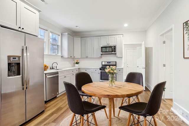 kitchen with backsplash, sink, light hardwood / wood-style flooring, ornamental molding, and appliances with stainless steel finishes