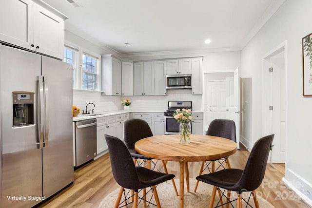 kitchen featuring decorative backsplash, appliances with stainless steel finishes, ornamental molding, sink, and light hardwood / wood-style flooring