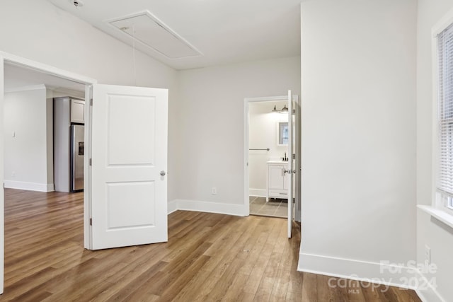 unfurnished bedroom featuring stainless steel fridge with ice dispenser, connected bathroom, and wood-type flooring