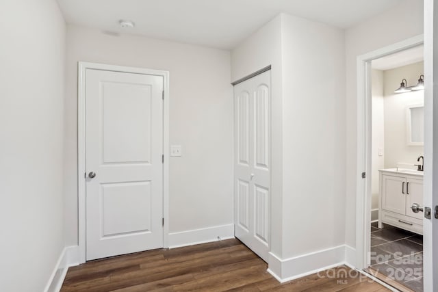 corridor with dark wood finished floors, a sink, and baseboards