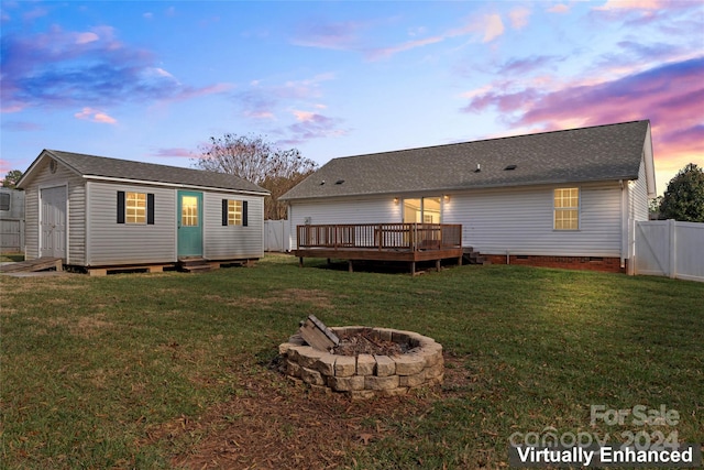 back house at dusk with a yard, a wooden deck, an outbuilding, and a fire pit