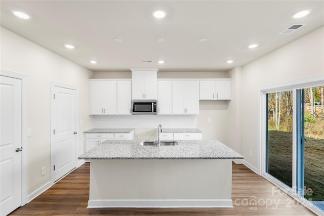 kitchen featuring light stone counters, a center island with sink, white cabinetry, and sink