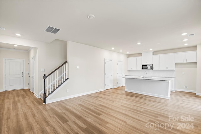 unfurnished living room featuring crown molding, sink, and light hardwood / wood-style flooring