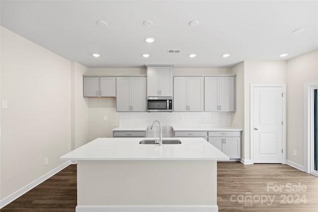 kitchen featuring tasteful backsplash, sink, an island with sink, and dark wood-type flooring