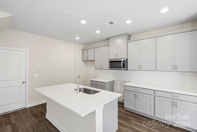 kitchen with gray cabinetry, sink, dark hardwood / wood-style floors, backsplash, and a kitchen island with sink