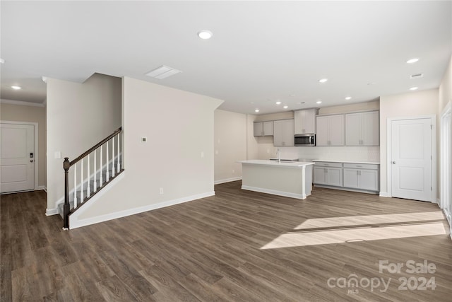 kitchen with sink, tasteful backsplash, crown molding, hardwood / wood-style floors, and a center island with sink