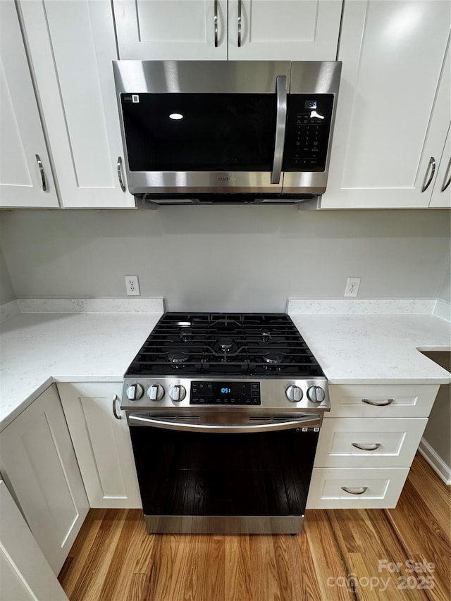 kitchen featuring white cabinetry, appliances with stainless steel finishes, light stone counters, and light wood-type flooring