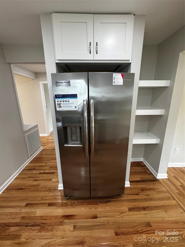 kitchen featuring wood-type flooring, stainless steel fridge, and white cabinets