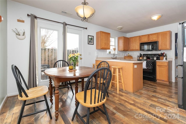 kitchen featuring tasteful backsplash, a breakfast bar, black appliances, decorative light fixtures, and dark hardwood / wood-style floors