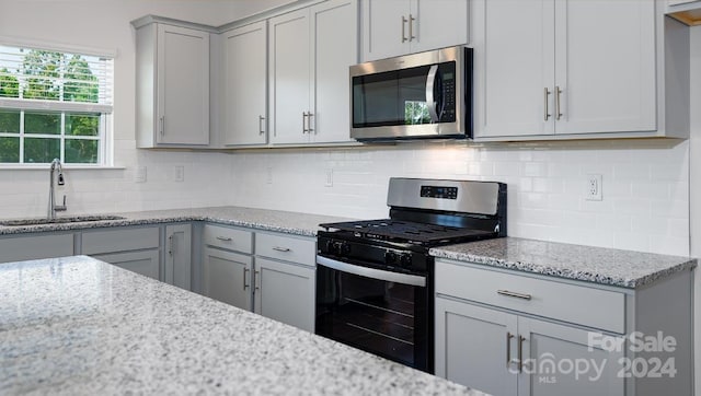 kitchen featuring tasteful backsplash, light stone counters, gray cabinetry, stainless steel appliances, and sink