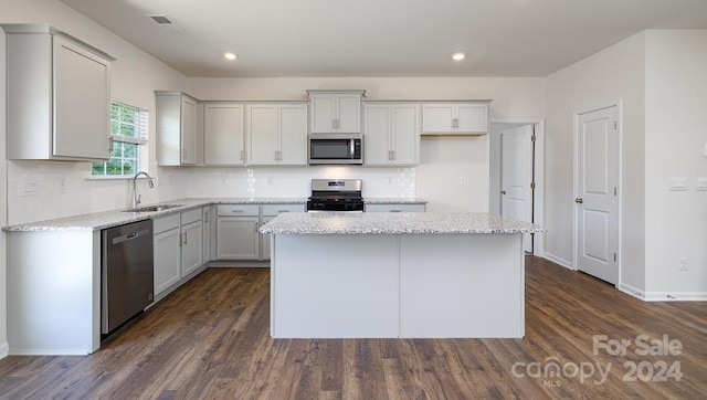 kitchen with light stone countertops, stainless steel appliances, sink, a center island, and dark hardwood / wood-style floors