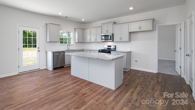 kitchen with dark wood-type flooring, sink, a kitchen island, light stone counters, and stainless steel appliances