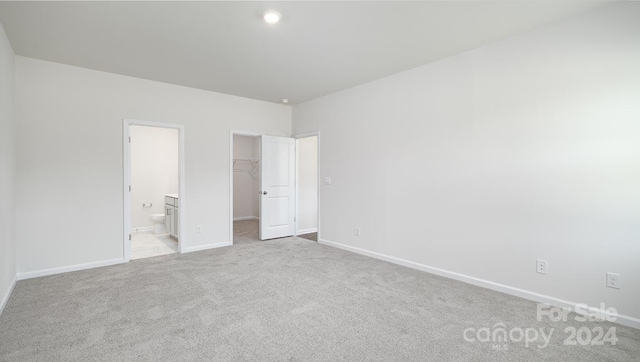 unfurnished bedroom featuring a closet, a spacious closet, ensuite bathroom, and light colored carpet