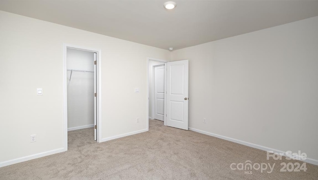 unfurnished bedroom featuring light colored carpet, a spacious closet, and a closet