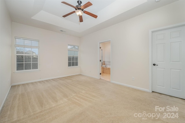 unfurnished bedroom featuring light carpet, connected bathroom, a tray ceiling, and ceiling fan