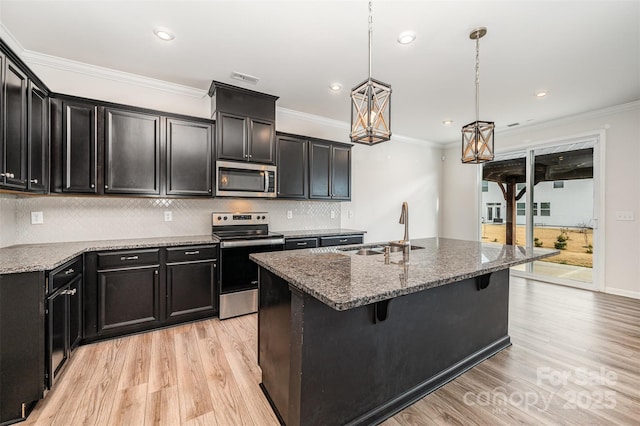 kitchen with a kitchen island with sink, appliances with stainless steel finishes, sink, stone countertops, and decorative light fixtures