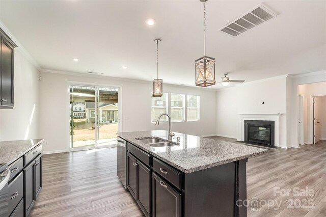 kitchen with sink, decorative light fixtures, stainless steel dishwasher, light stone countertops, and a center island with sink