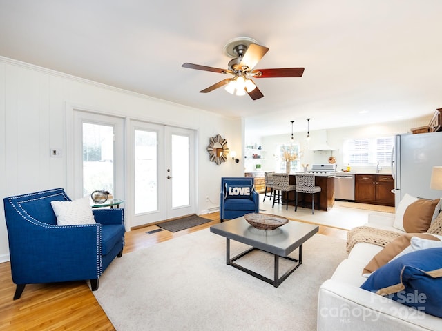 living room featuring ceiling fan, french doors, sink, crown molding, and light wood-type flooring