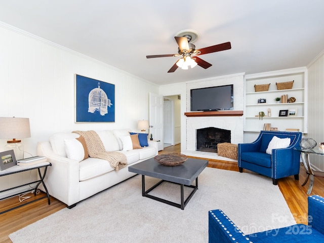 living room with light hardwood / wood-style floors, built in features, crown molding, and a brick fireplace