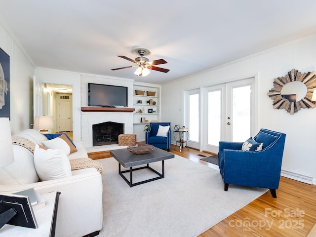 living room with hardwood / wood-style floors, built in shelves, ceiling fan, ornamental molding, and a fireplace