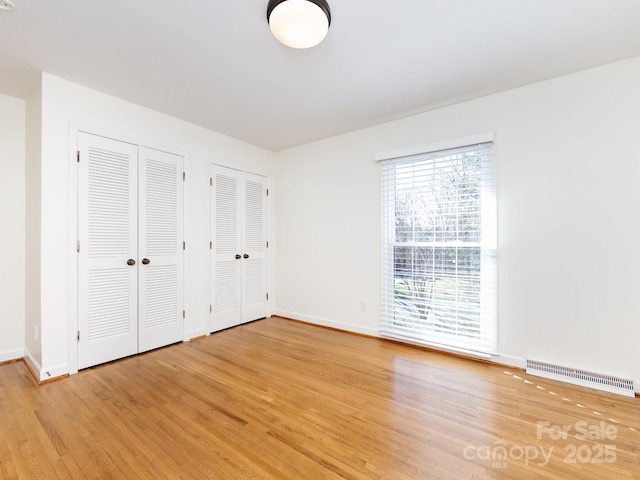 unfurnished bedroom with multiple closets and light hardwood / wood-style flooring