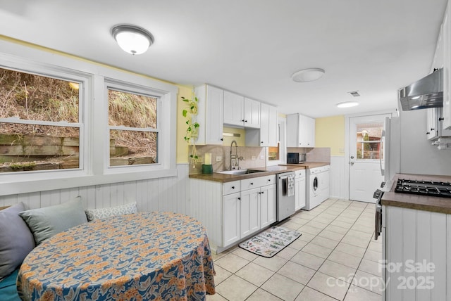 kitchen featuring ventilation hood, sink, stainless steel dishwasher, white cabinetry, and washer / clothes dryer