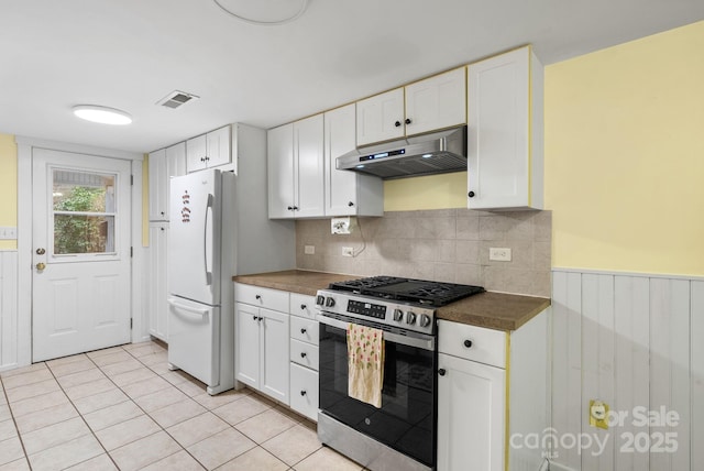 kitchen with stainless steel gas range oven, light tile patterned flooring, white refrigerator, decorative backsplash, and white cabinets