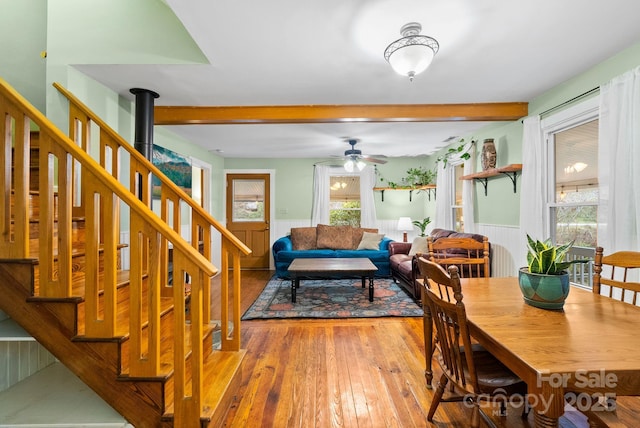 dining space featuring ceiling fan, beam ceiling, wood-type flooring, and a wood stove