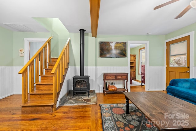 living room featuring beam ceiling, hardwood / wood-style flooring, a wood stove, and ceiling fan