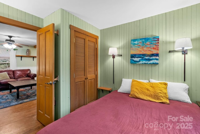 bedroom featuring hardwood / wood-style floors, a closet, ceiling fan, and wooden walls